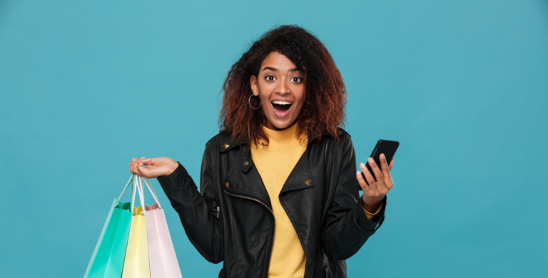 African lady excited on a blue background holding shopping bags and her phone