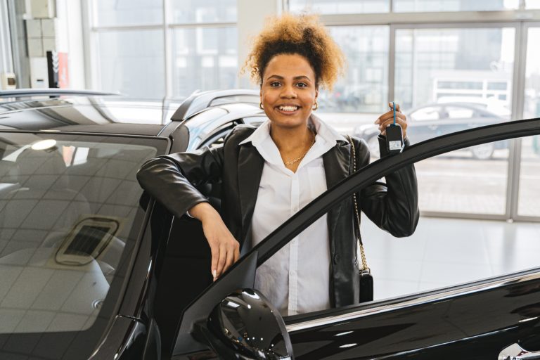 Black lady standing near a black car holding keys