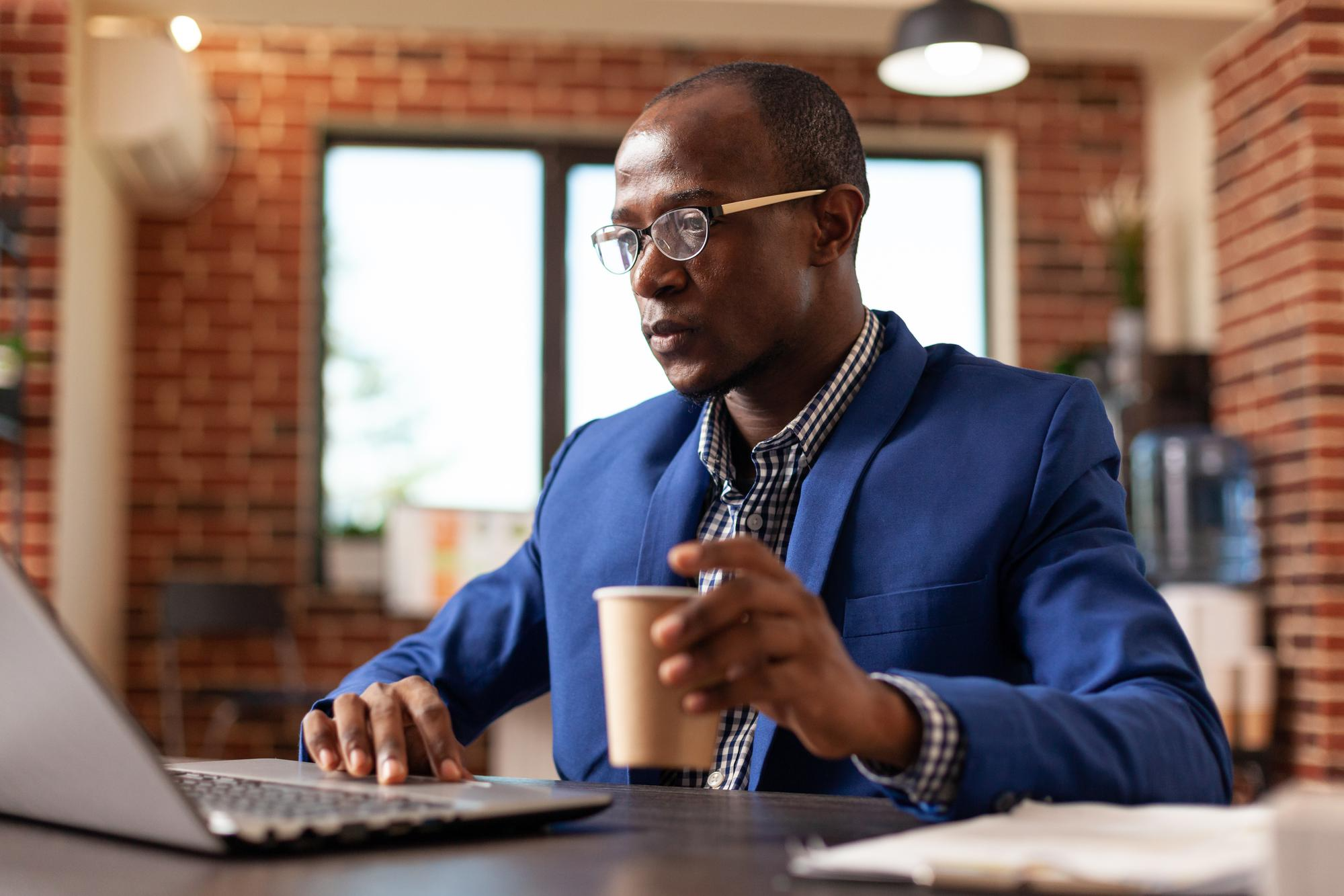 African Man in a blue suit holding a cup and on a laptop